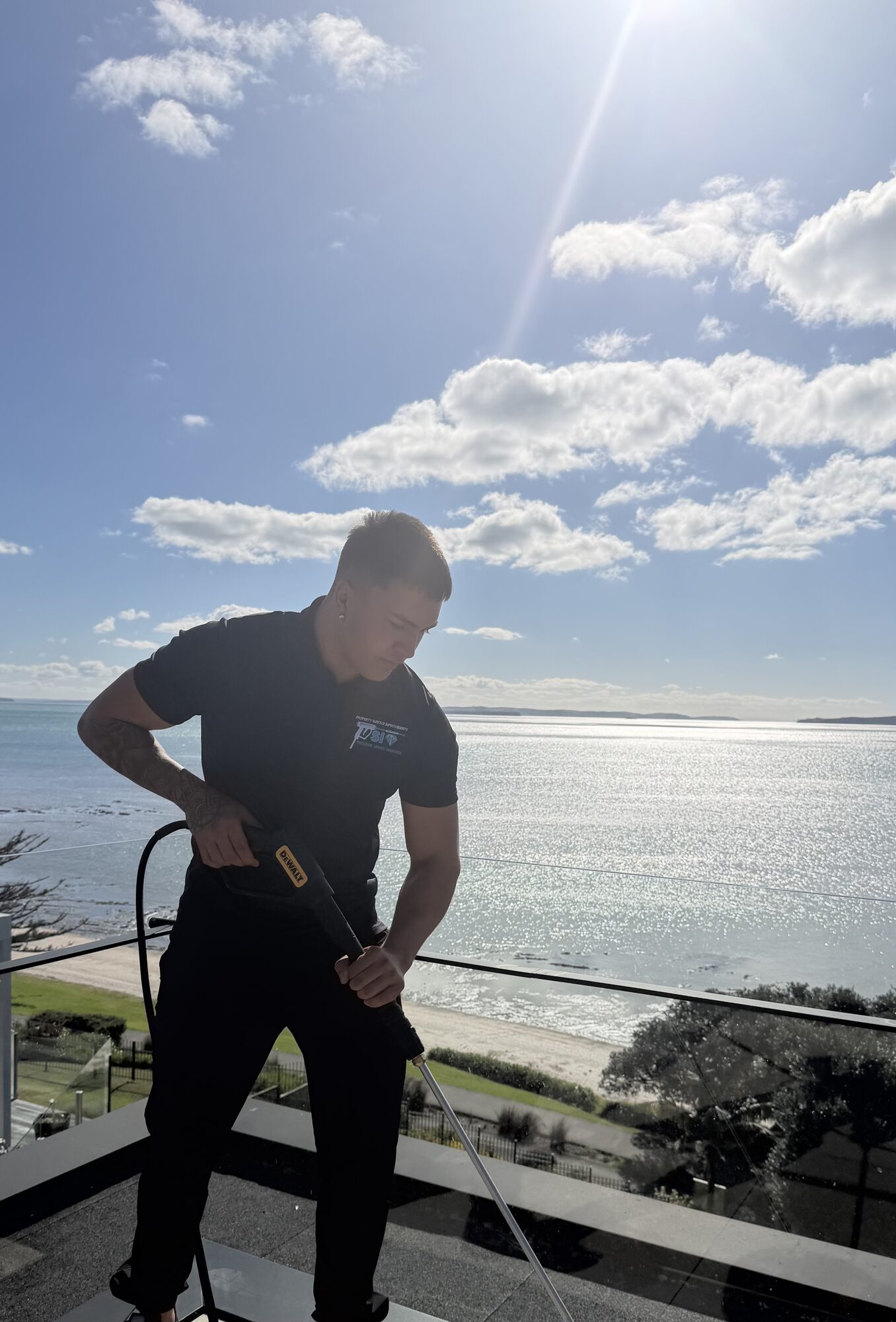 PSI operator soft washing with a pressure lance, Auckland coastline behind